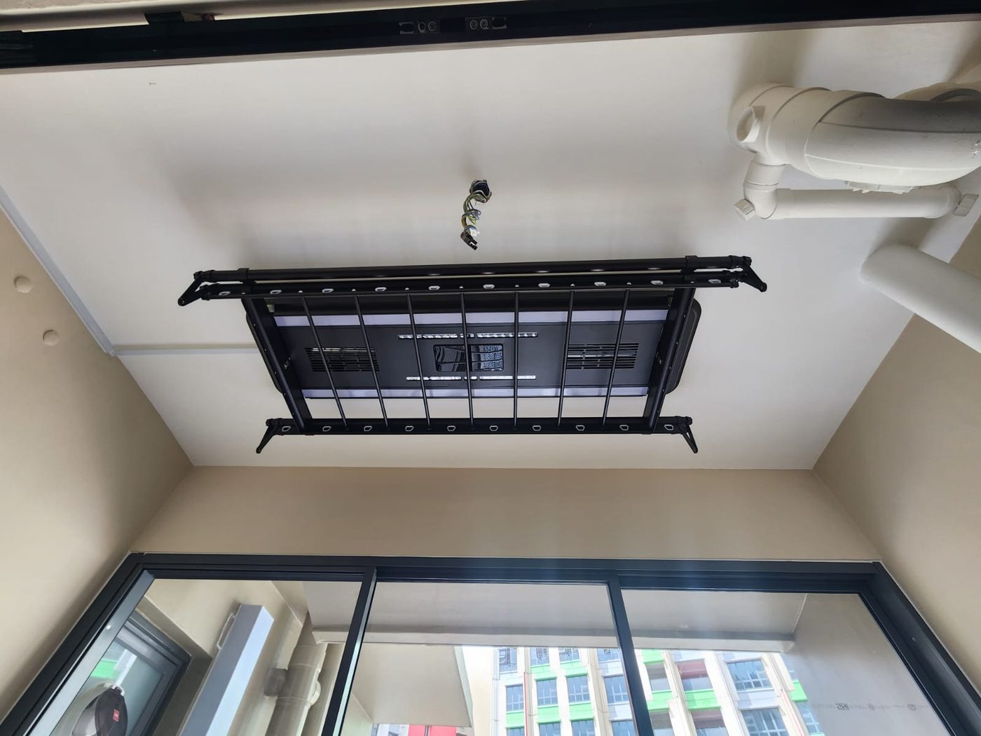 Black automated laundry rack installed on an HDB service yard ceiling, wired to the existing light point